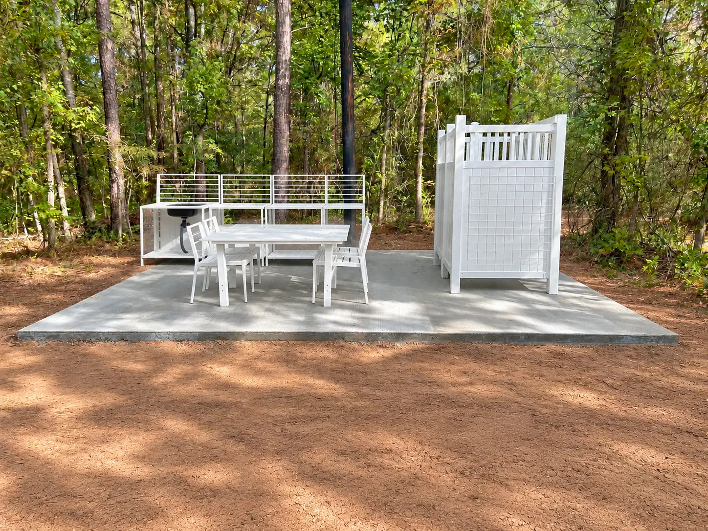 White outdoor kitchenette and dining area with a private shower stall among the pines